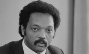 Jesse_Jackson_half-length_portrait_of_Jackson_seated_at_a_table_July_1_1983_edit.jpg-e1771338486931-300x182.webp.webp